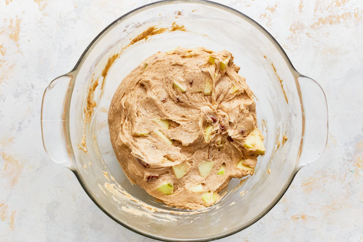 Gluten-free apple cake batter with apples and pecans in a glass mixing bowl.