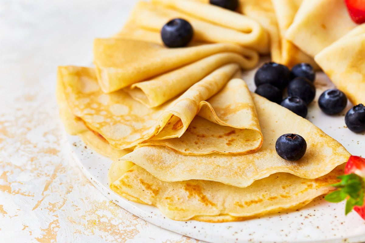 side view of triangles of gluten-free crepes arranged on a platter with blueberries and strawberries.