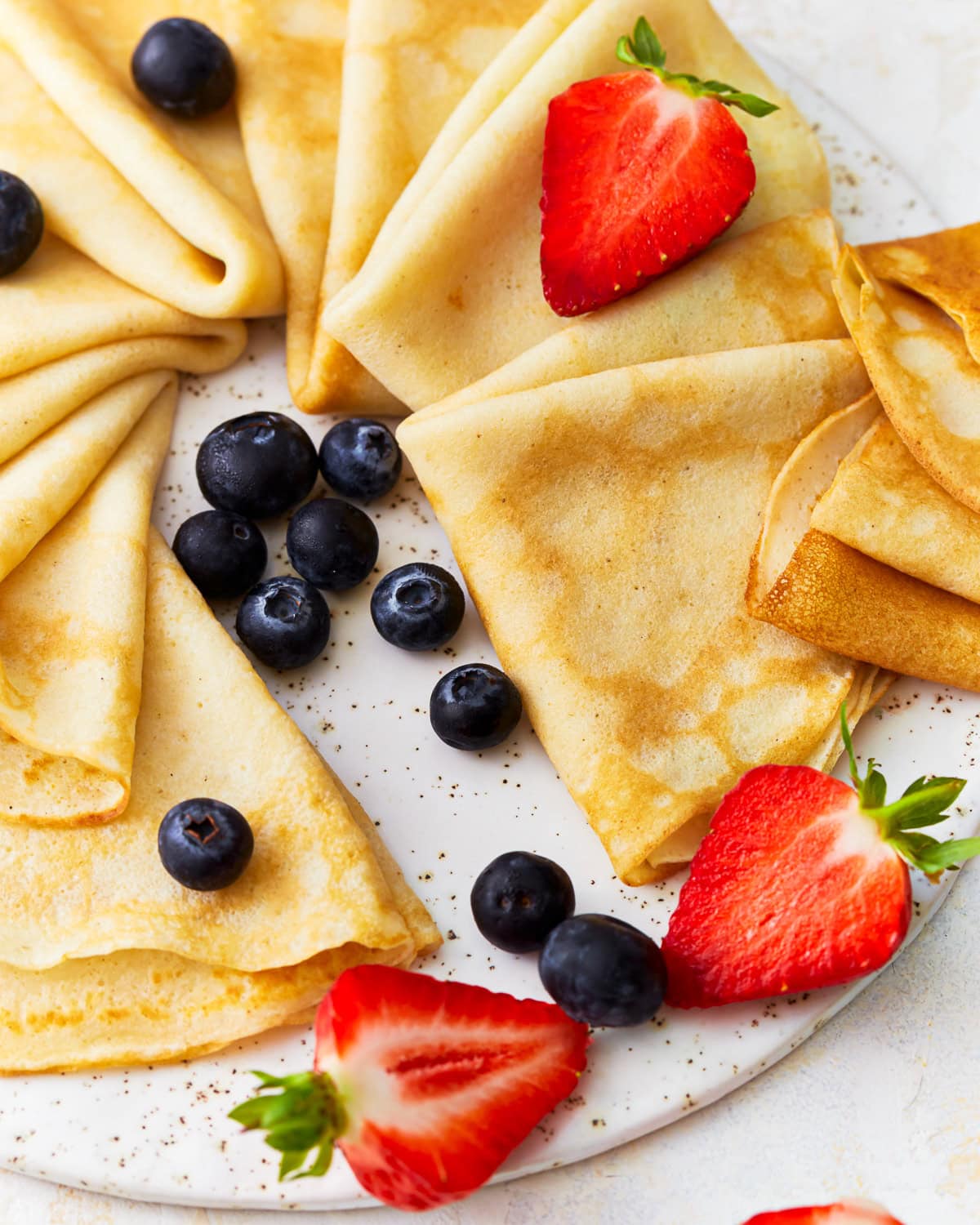 triangles of gluten-free crepes arranged on a platter with fresh fruit.