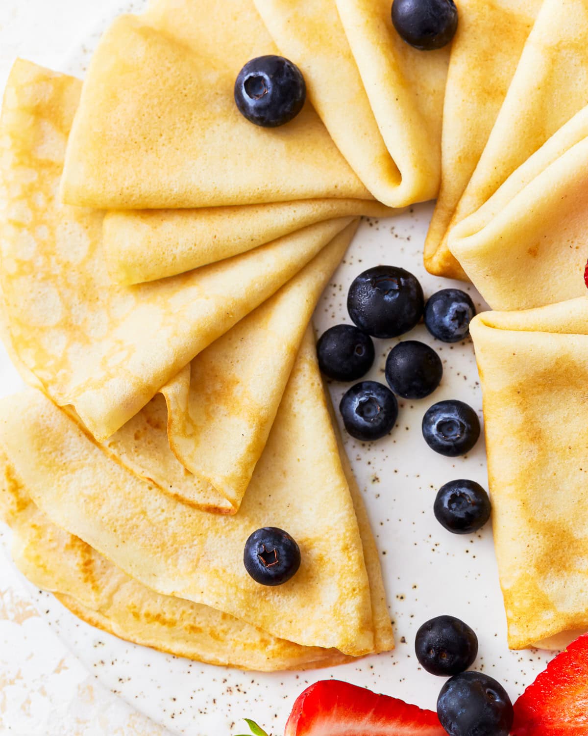 triangles of gluten-free crepes arranged on a platter with blueberries.