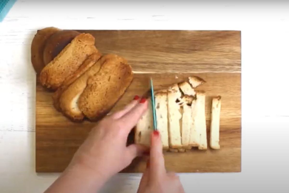 A hand slicing gluten-free bread on a chopping board for croutons.