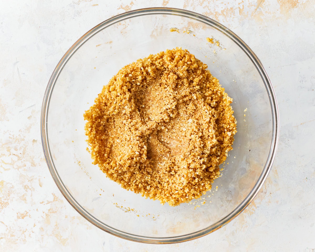 Mixture for gluten-free graham cracker crust in a glass mixing bowl.