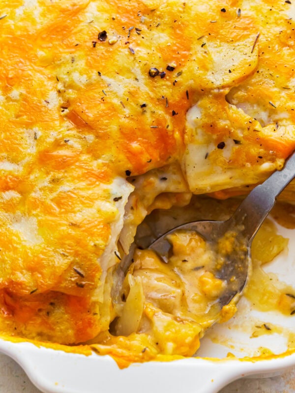 Overhead view of a spoon scooping gluten-free scalloped potatoes from a baking dish.