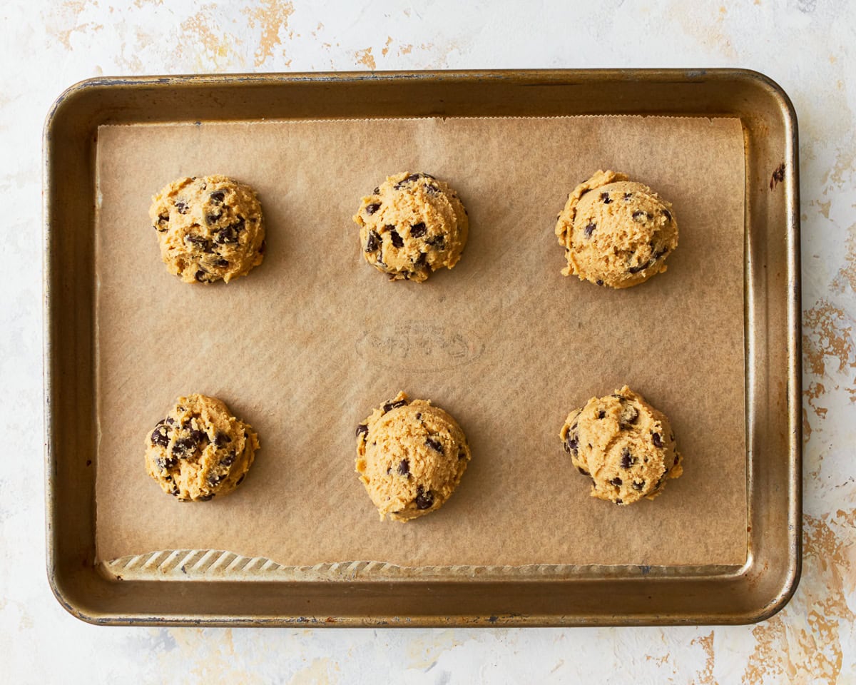 Gluten-free chocolate chip cookie dough balls on a parchment linked baking sheet.