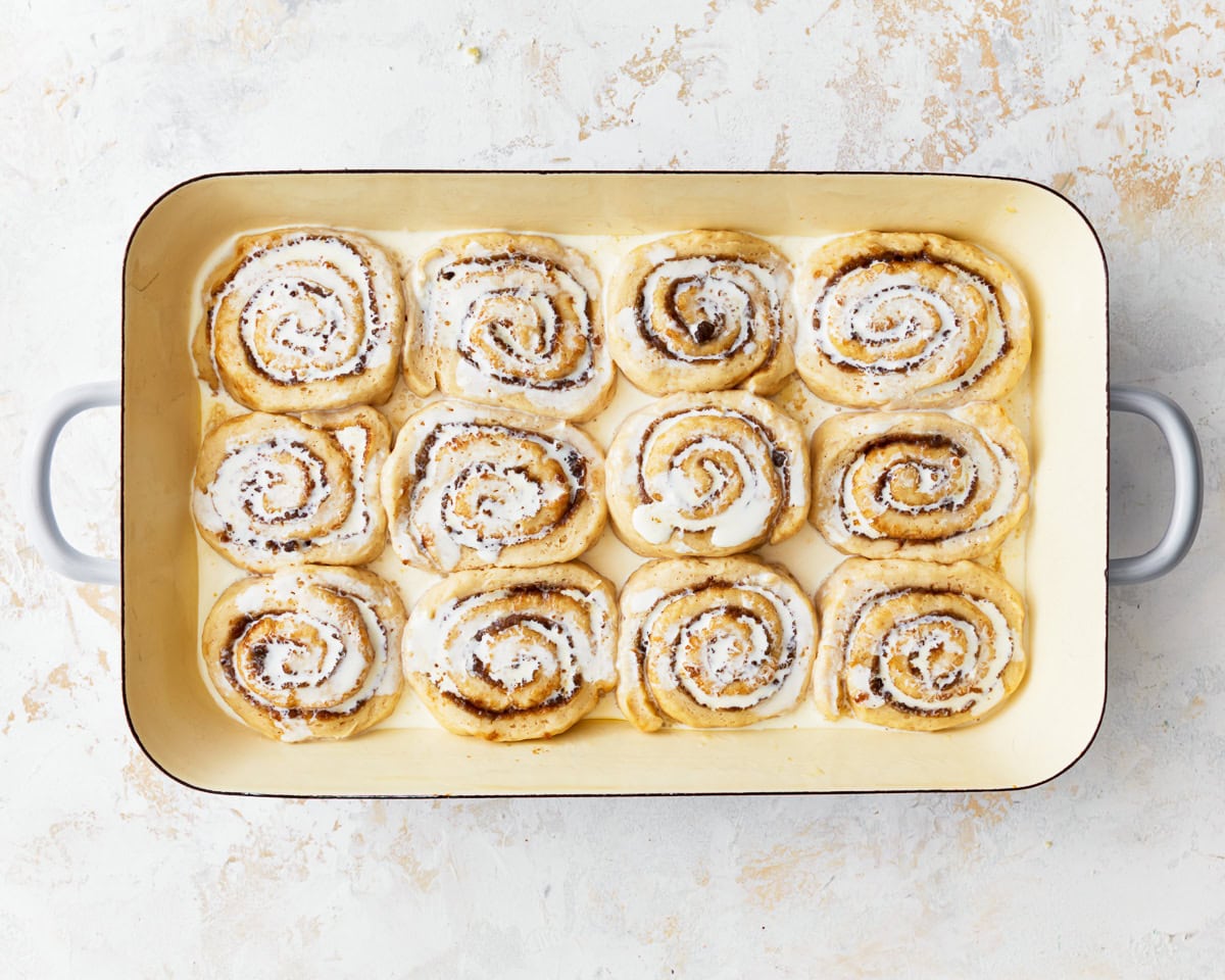 cream poured over unbaked cinnamon rolls in a tray.