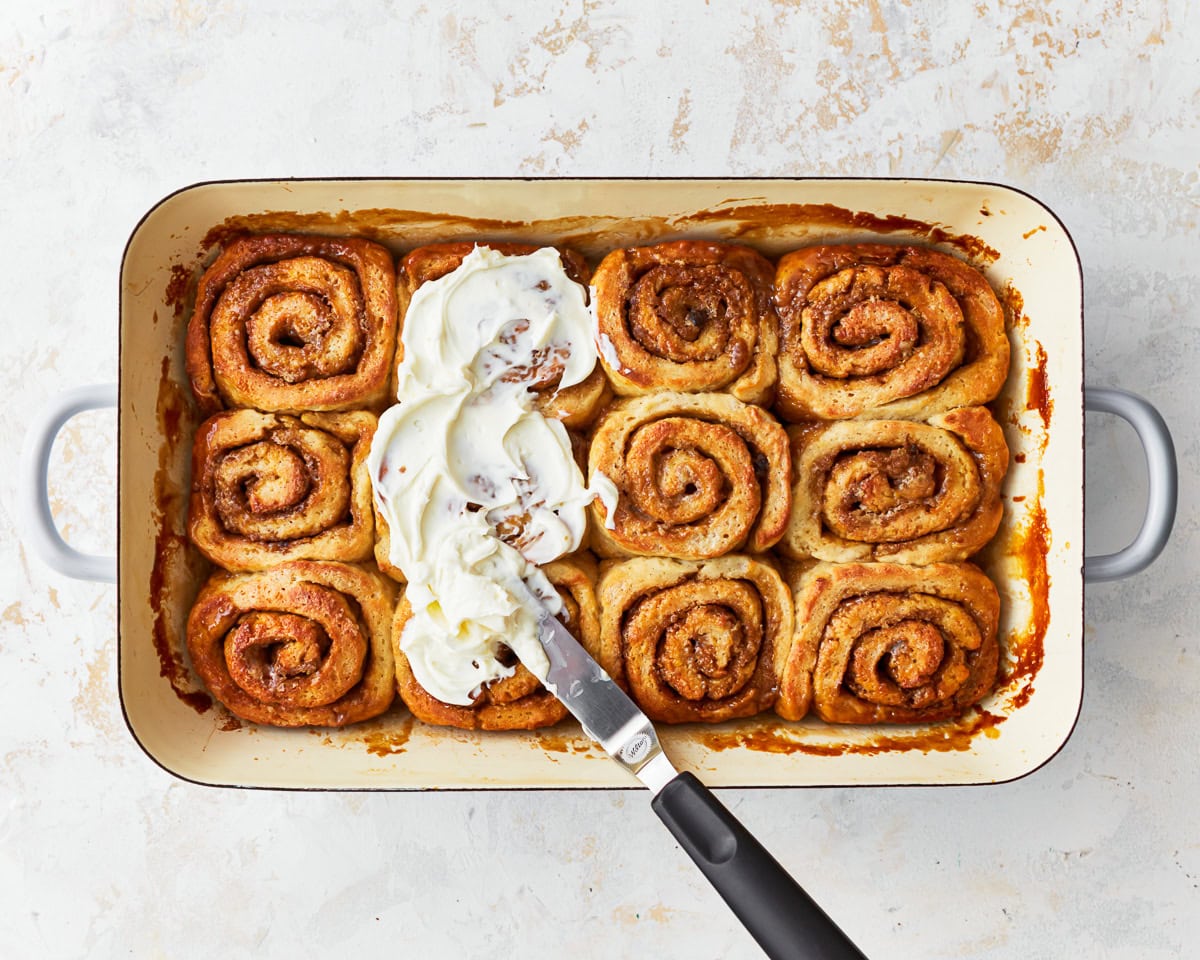 spreading frosting over gluten-free cinnamon rolls with an offset spatula.