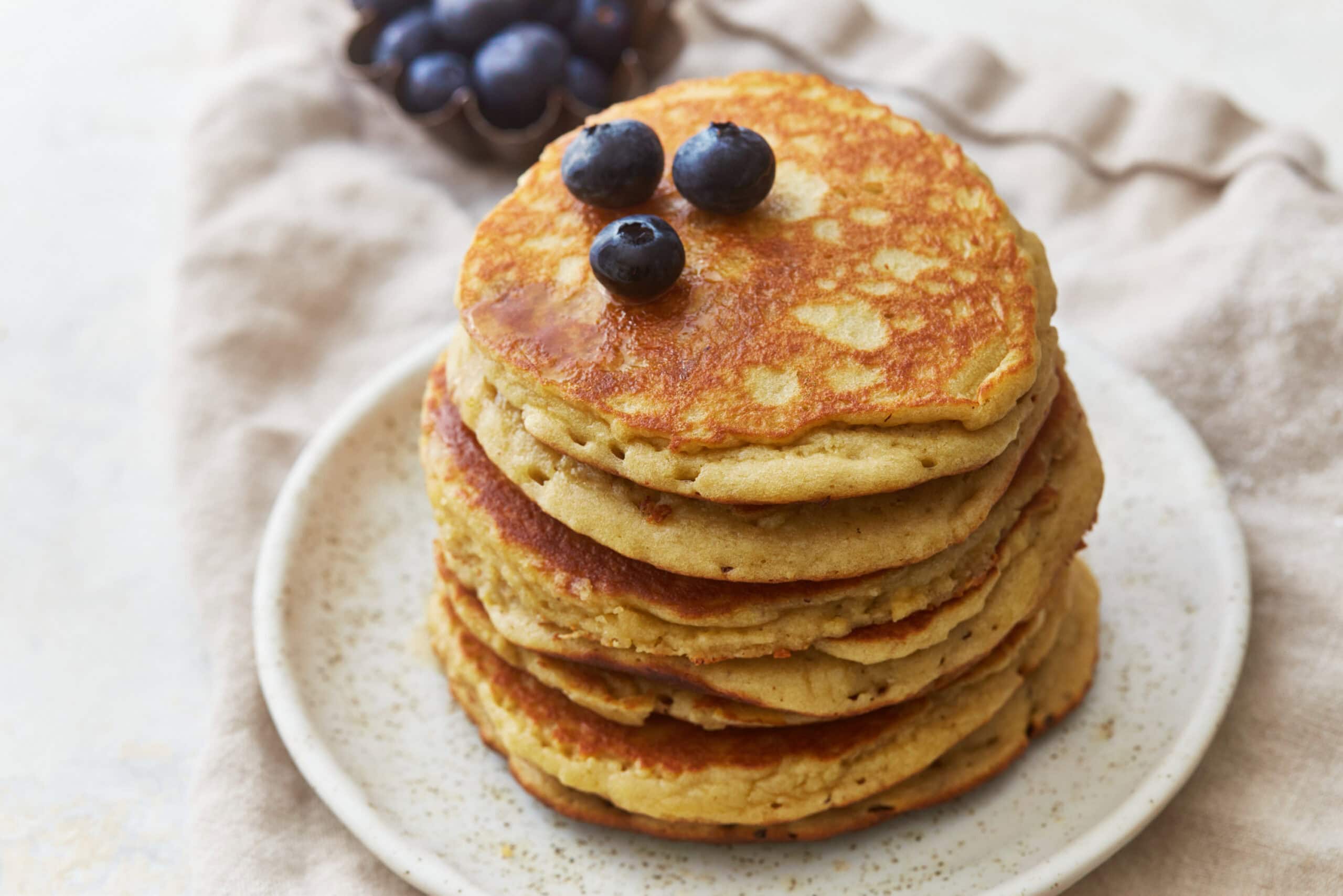three-quarters view of a stack of almond flour pancakes on a plate with blueberries.