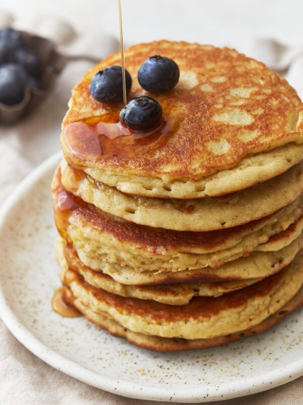 three-quarters view of a stack of almond flour pancakes on a plate with blueberries and syrup.