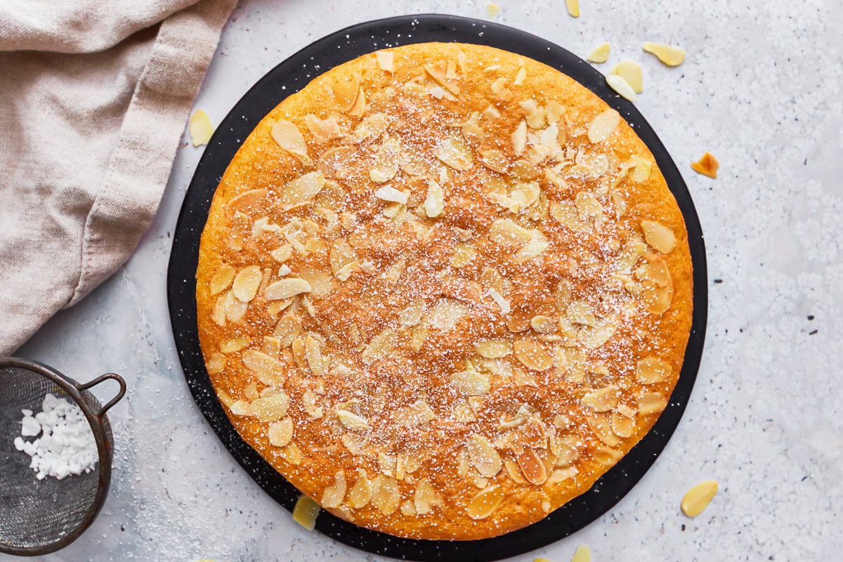 An almond flour cake topped with powdered sugar on a serving tray.