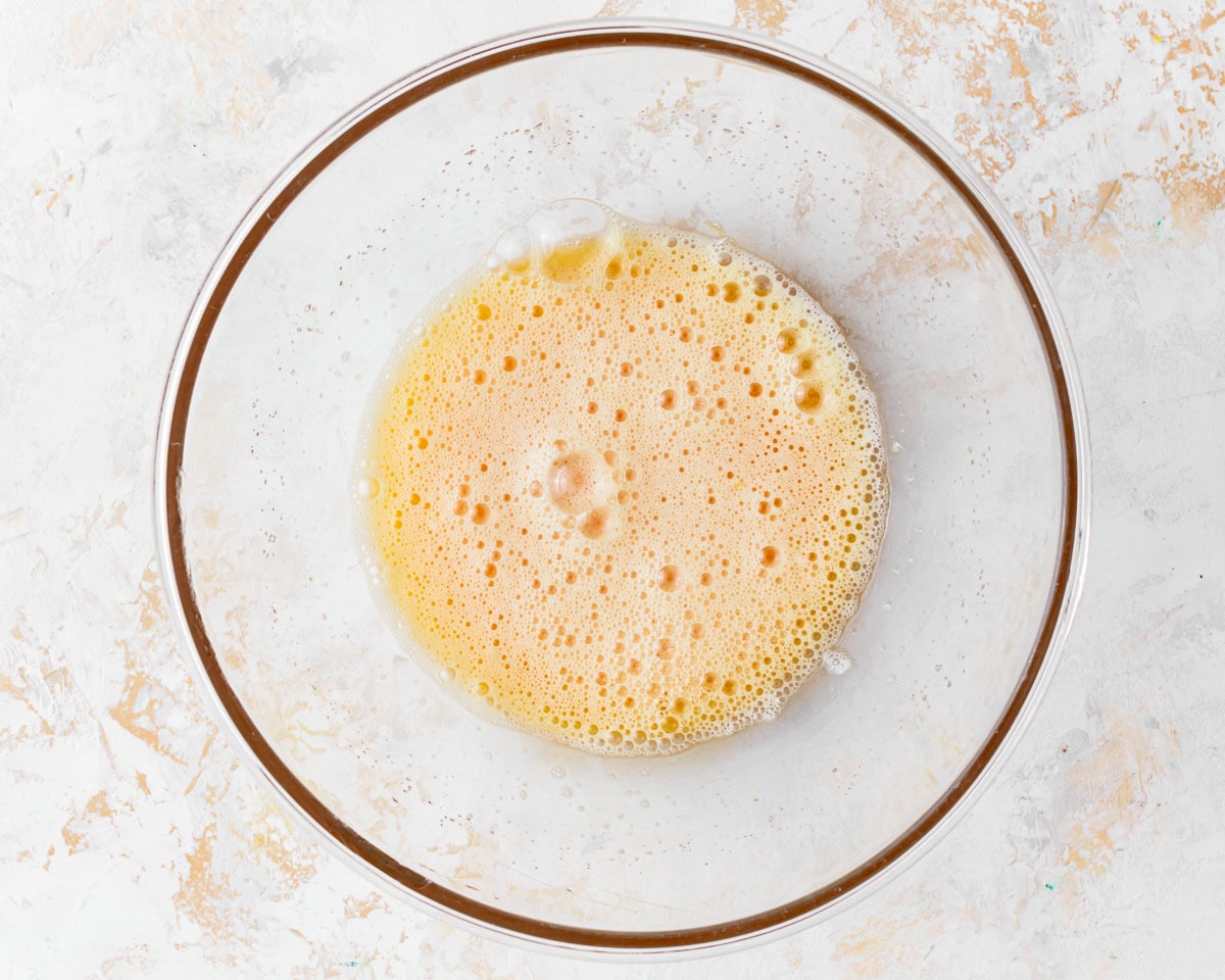 Beaten eggs and sugar in a glass mixing bowl.