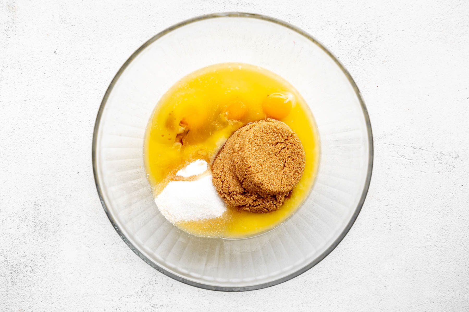 Eggs and sugar in a glass mixing bowl.