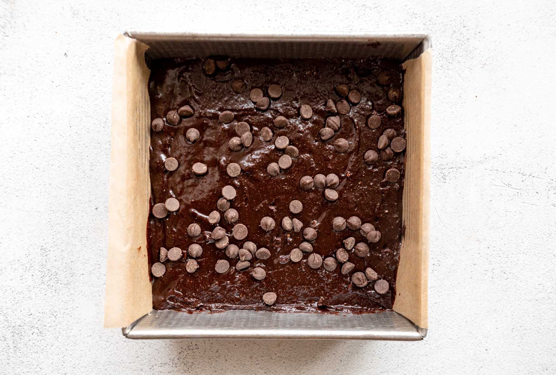 Almond flour brownie batter in a baking pan topped with chocolate chips