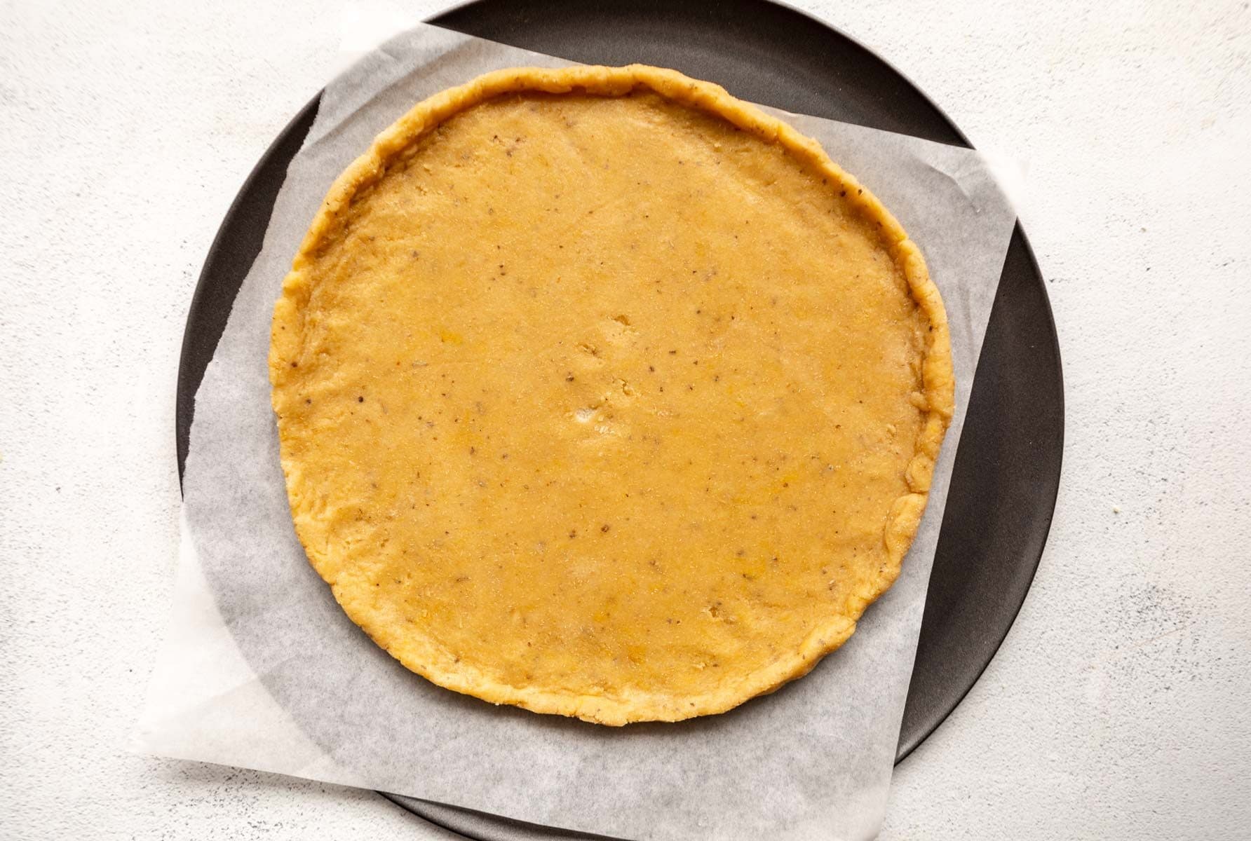 almond flour pizza dough rolled into a circle on a parchment lined pizza pan.