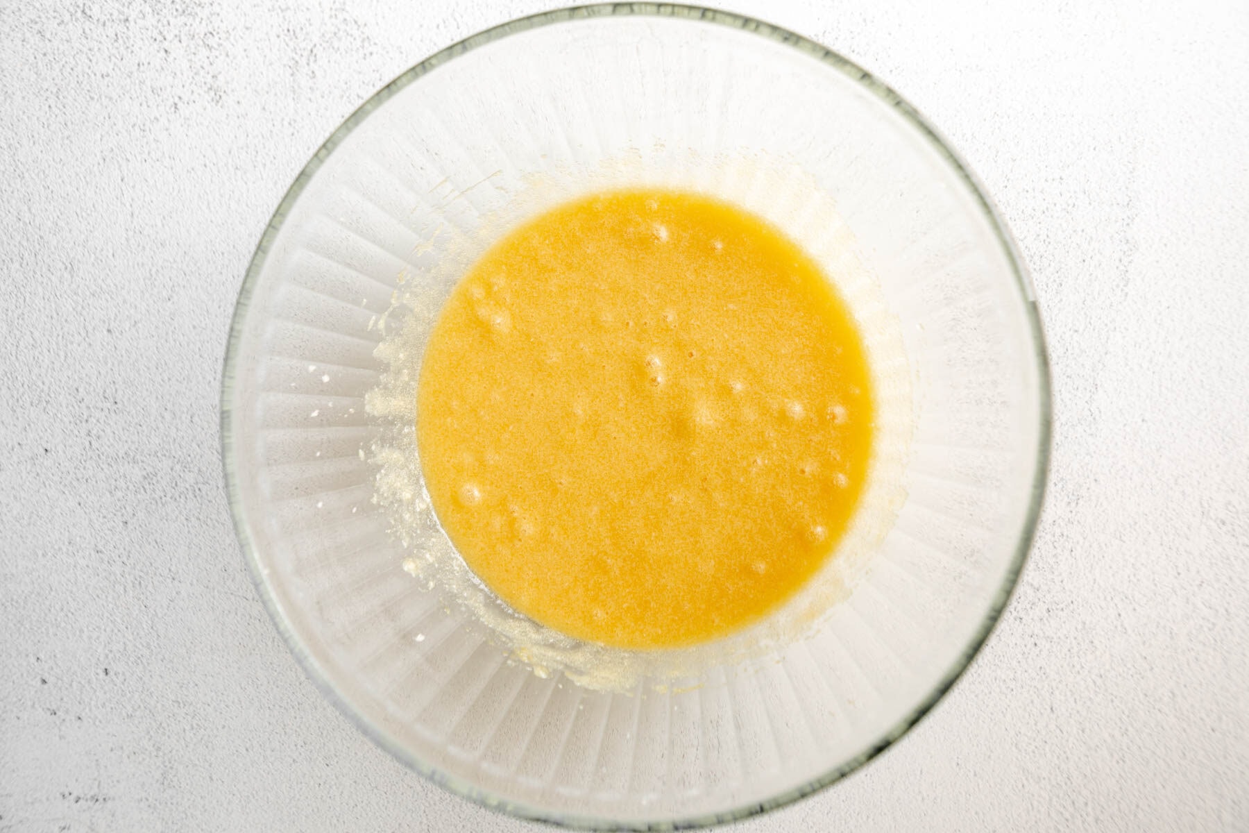 Eggs and vanilla added to creamed butter and sugar in a glass mixing bowl.