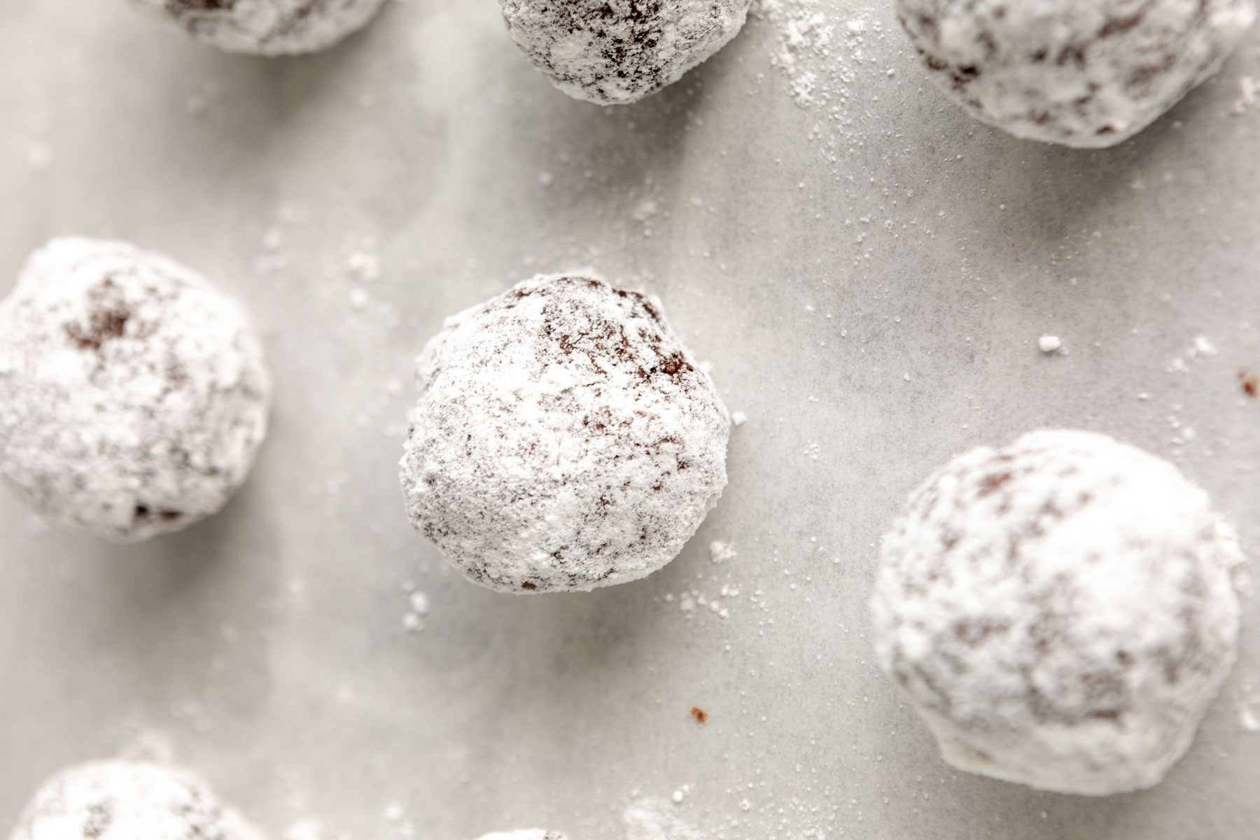 Gluten-free chocolate crinkle cookie dough balls rolled in powdered sugar.