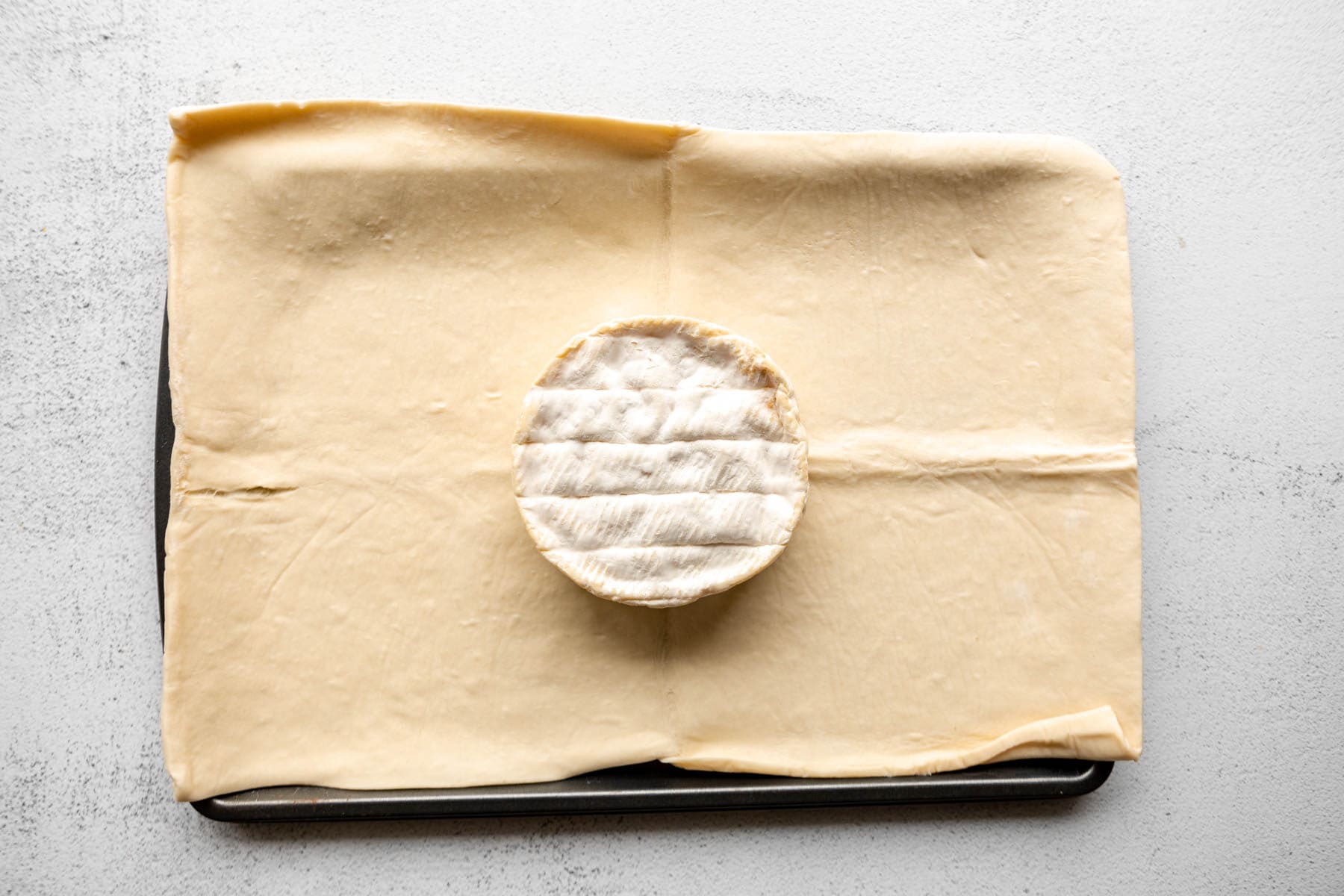 A wheel of brie on a gluten-free puff pastry sheet.