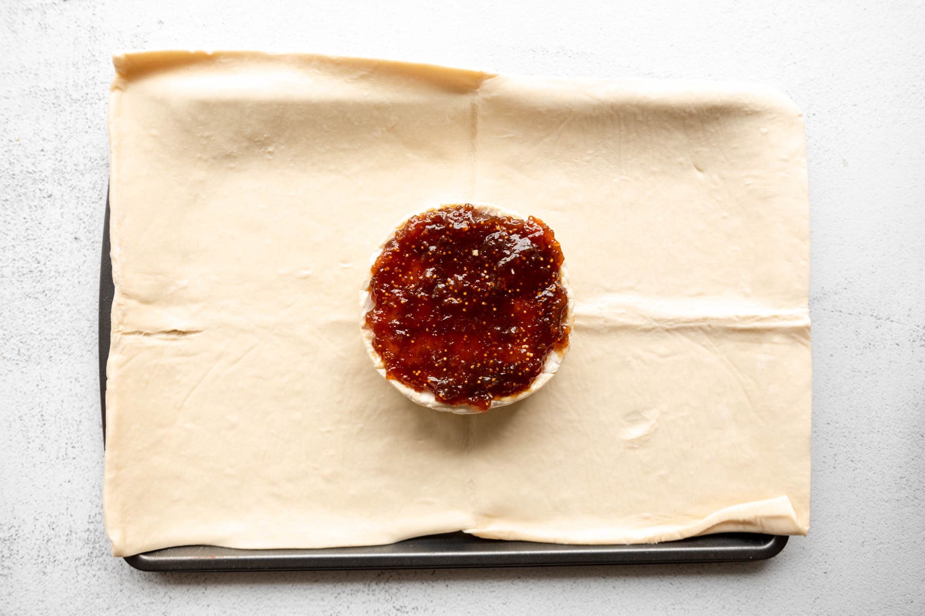 A wheel of brie topped with fig jam on a sheet of gluten-free puff pastry.