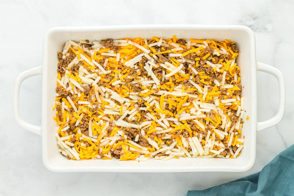 hash browns, cheese, and crumbled cooked sausage in a baking pan.