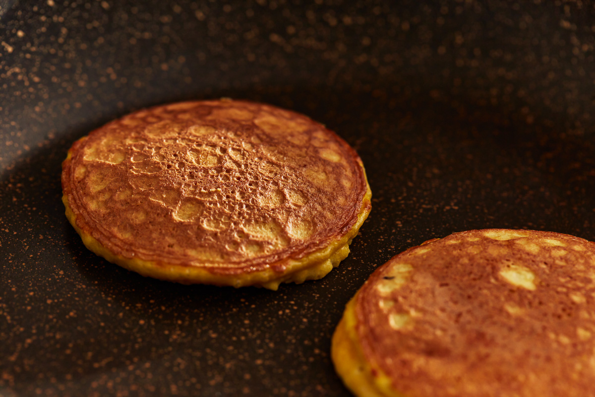 coconut flour pancakes cooking on a griddle.