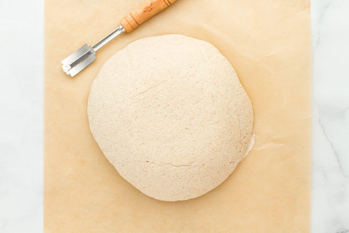 risen gluten free sourdough bread on a cutting board with a lame.