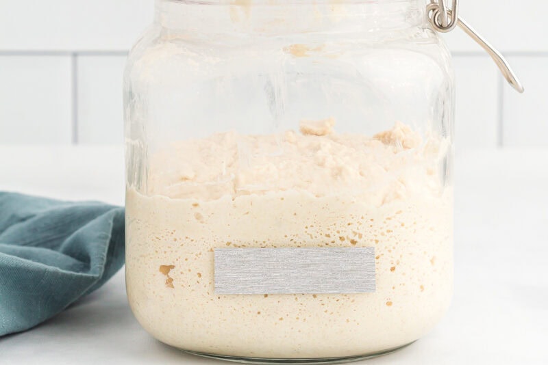 gluten free sourdough starter in a glass jar with tape on the side.