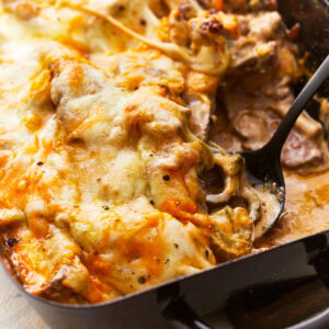 close up of a spoon scooping philly cheesesteak casserole from a casserole dish.