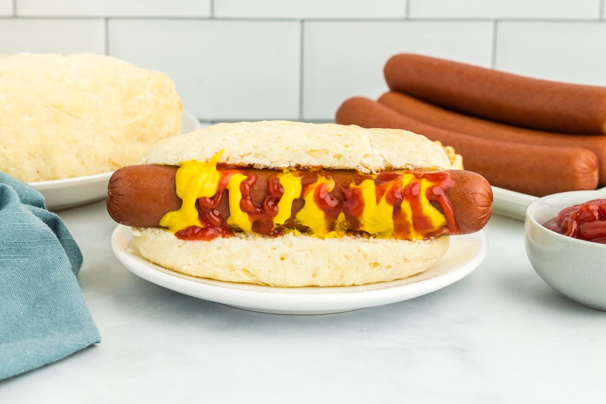 a gluten-free hot dog bun with a hot dog topped with ketchup and mustard on a white plate.