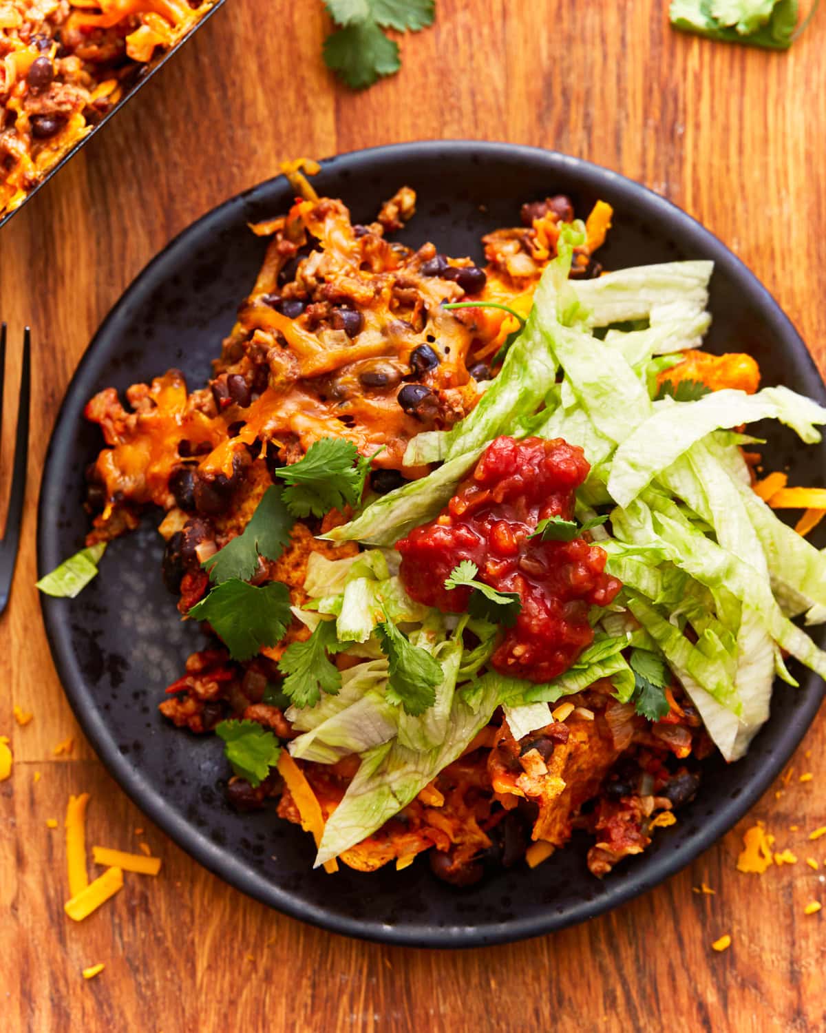 a serving of walking taco casserole on a plate with lettuce and salsa.
