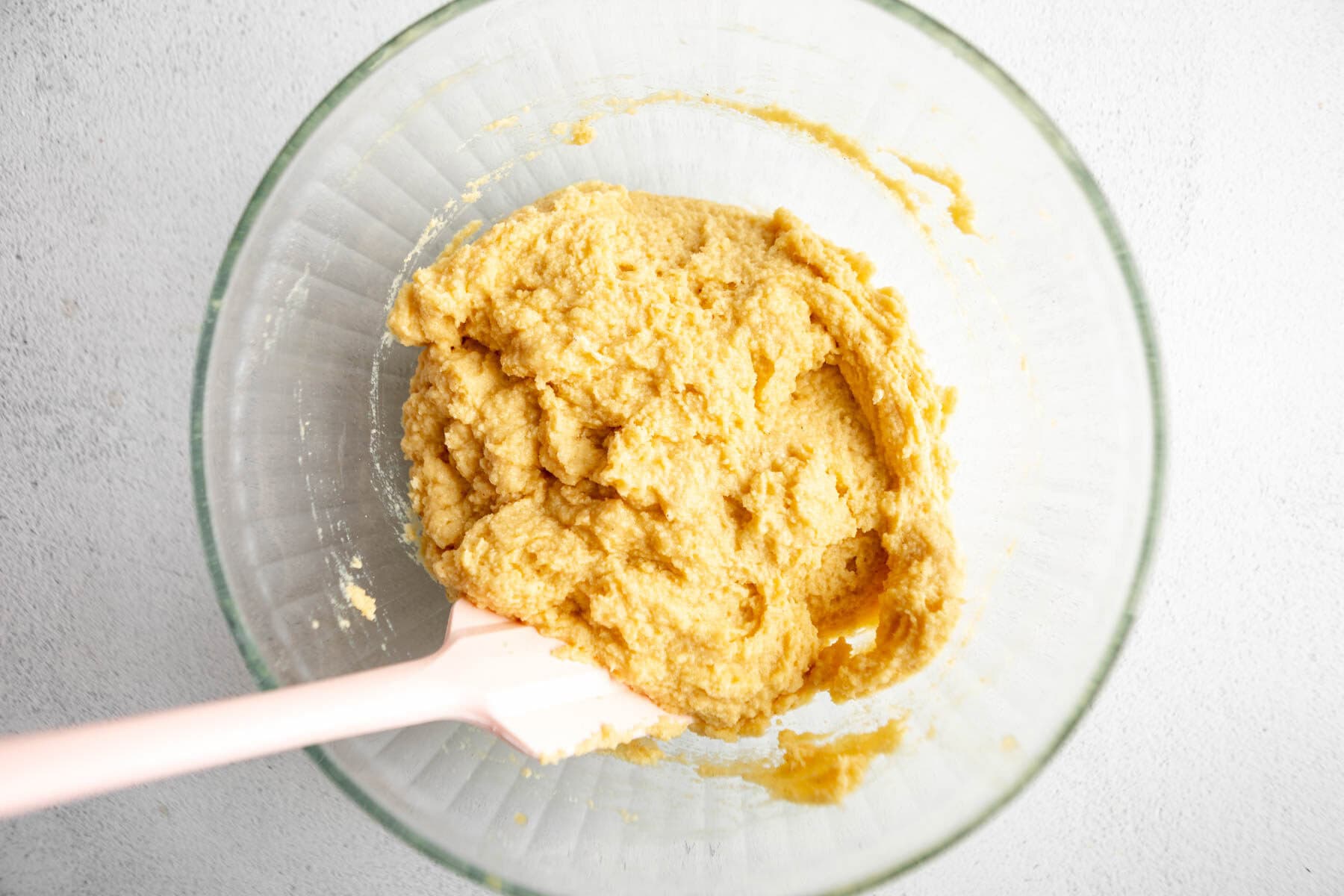 coconut flour bread dough in a glass bowl with a rubber spatula.