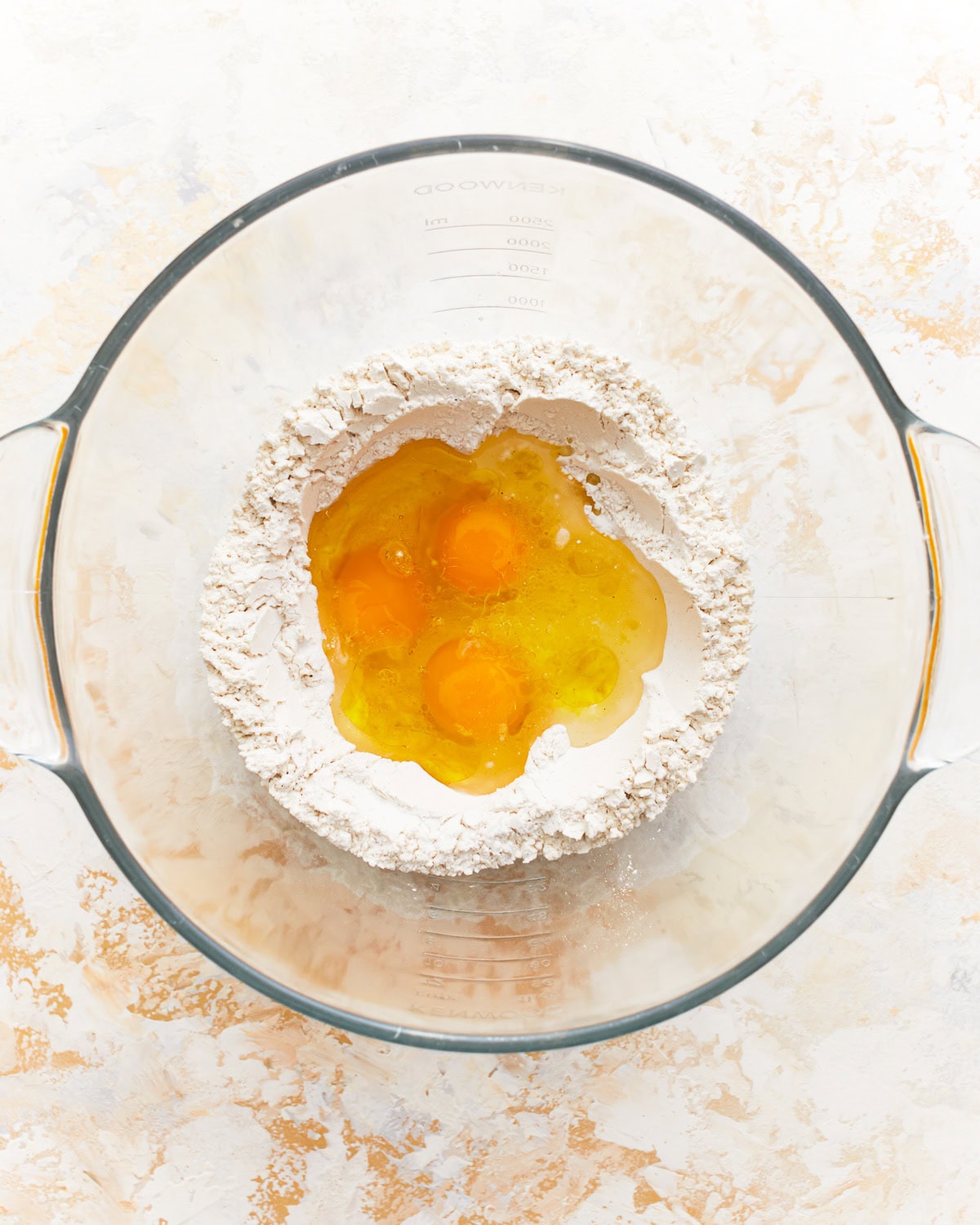 eggs in the center of a flour well in a glass bowl.