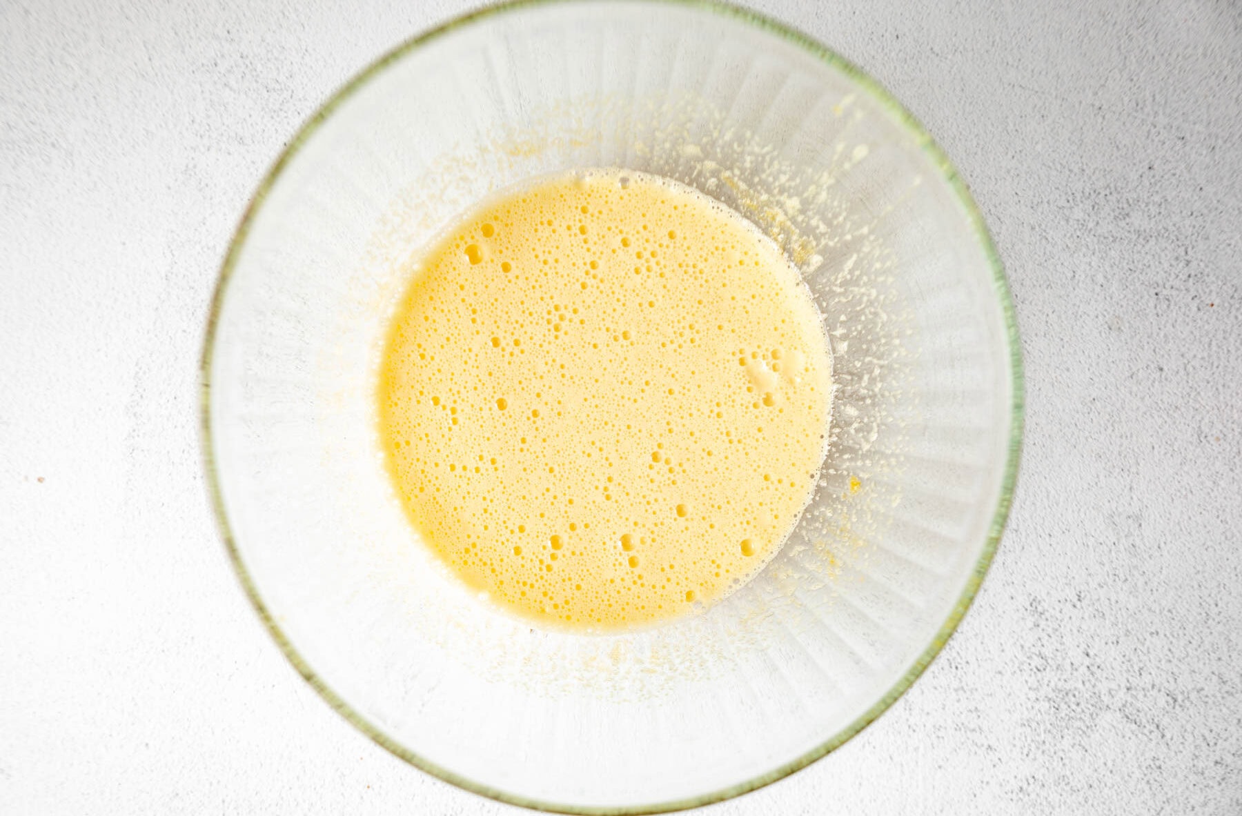 Whisked eggs and sugar for coconut flour brownies in a glass mixing bowl.