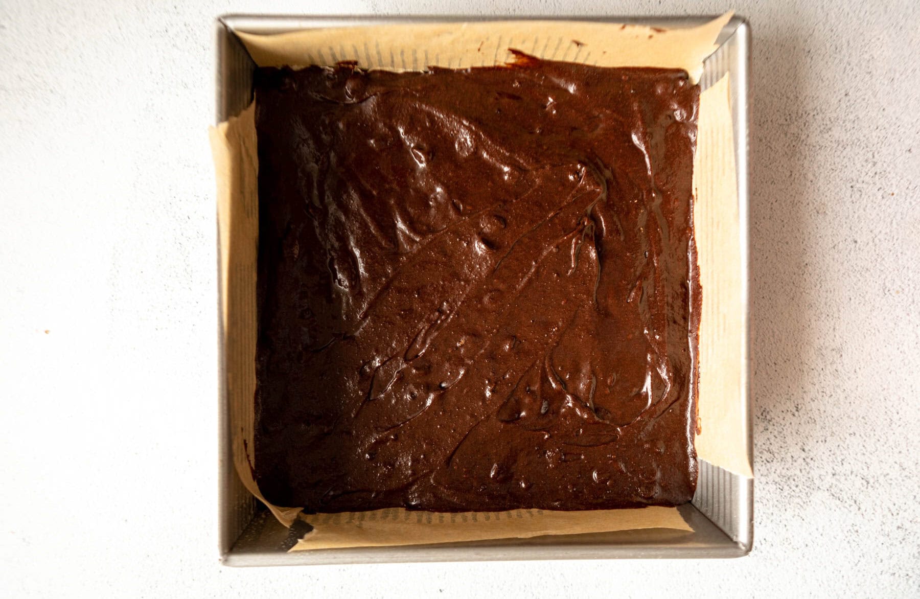 Brownie batter for coconut flour brownies in a parchment lined baking pan.