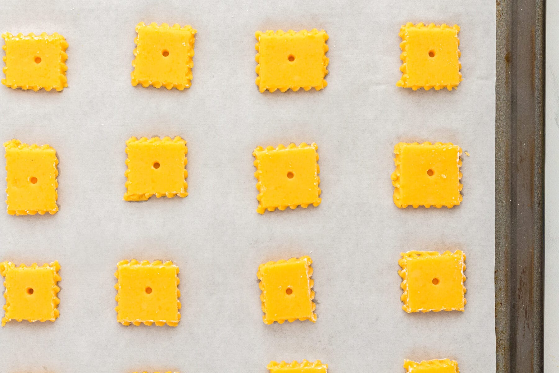 Uncooked gluten free cheez its crackers on a parchment lined baking sheet.