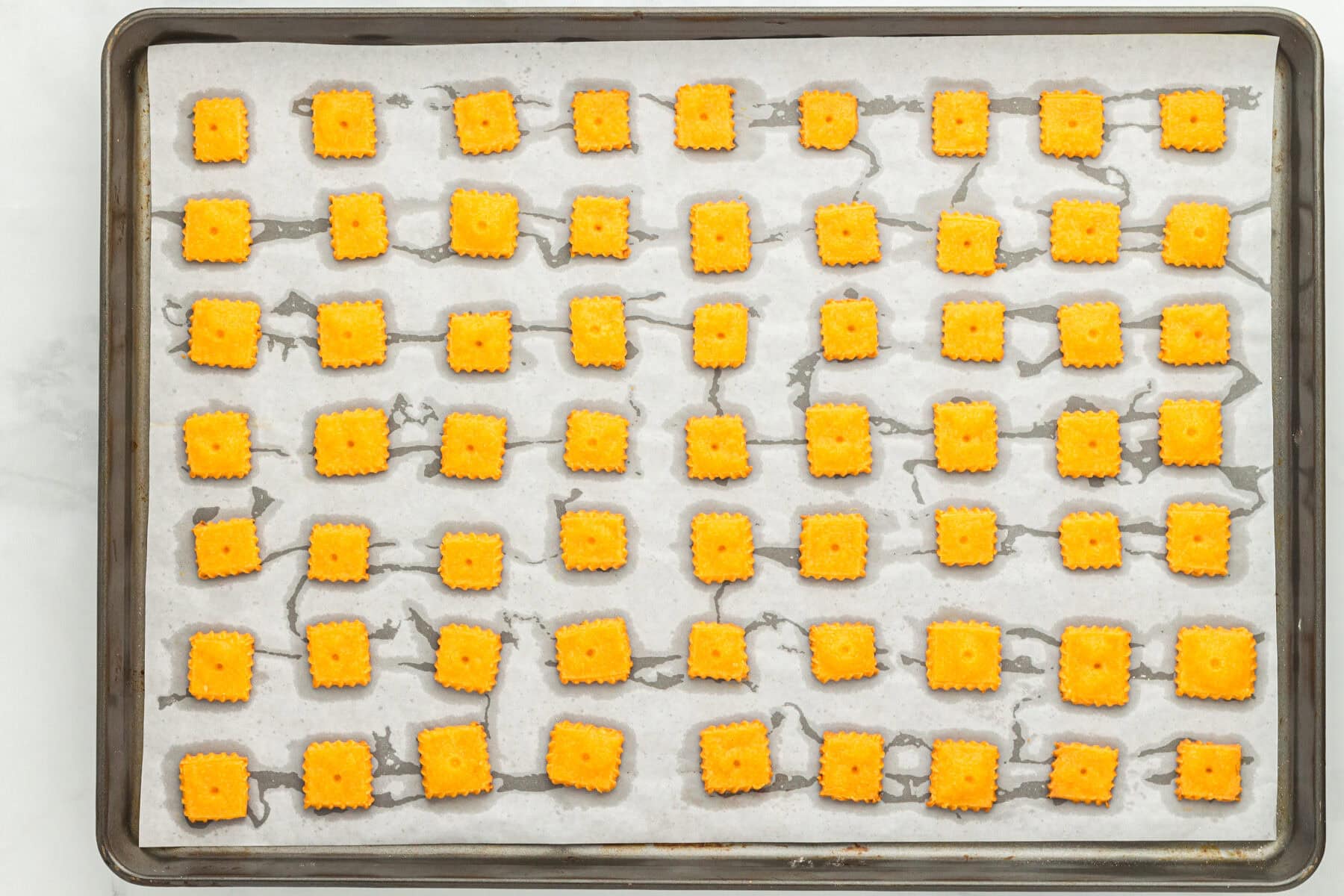 Overhead view of gluten free cheez its on a parchment lined baking sheet.