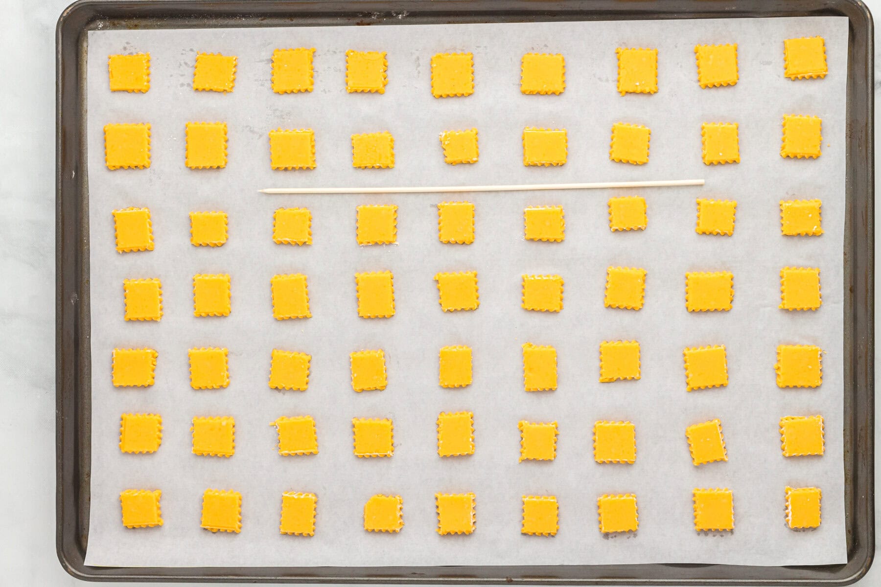 Uncooked gluten free cheez its on a parchment lined baking sheet.