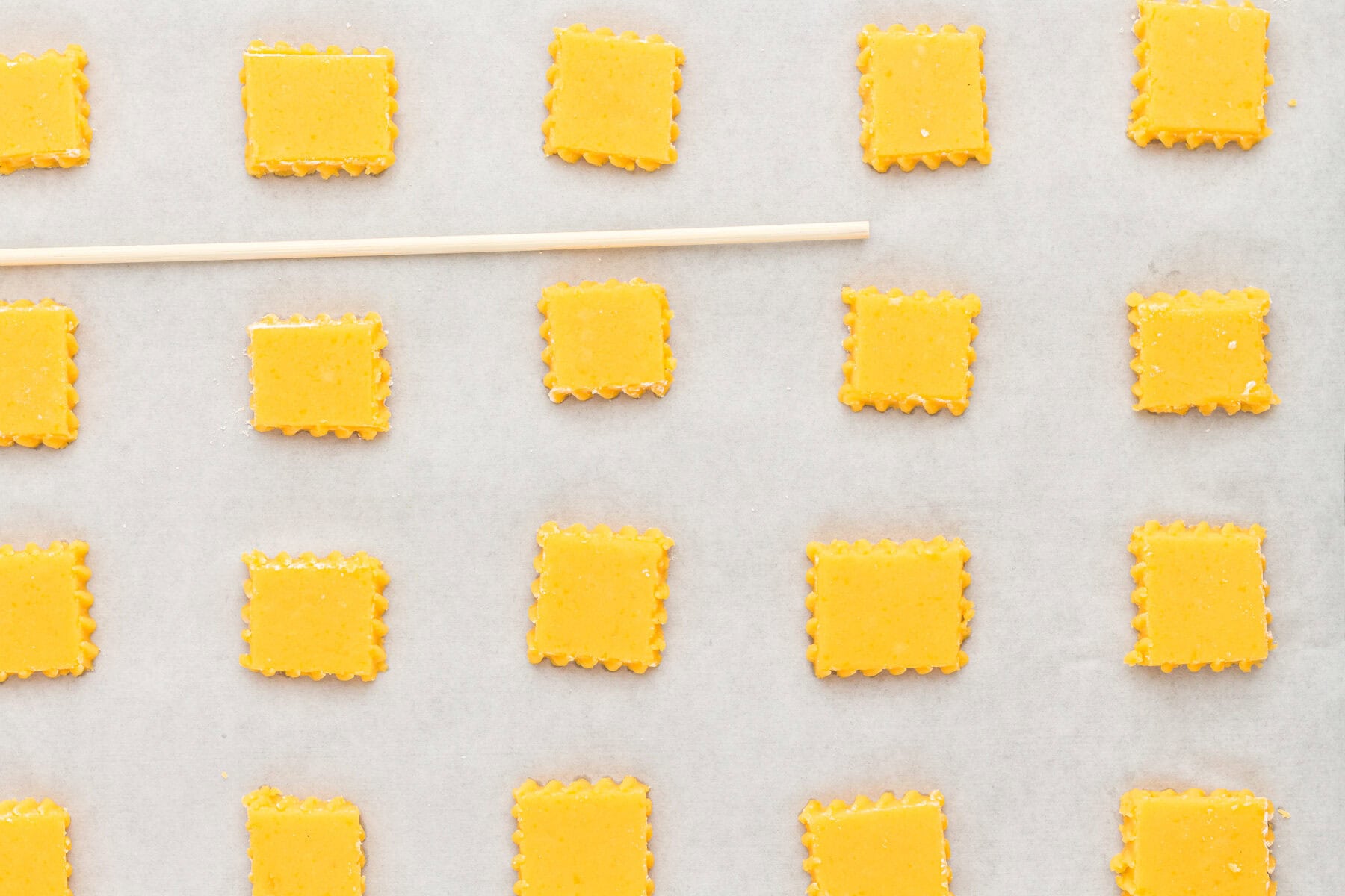 Uncooked gluten free cheez its on a parchment lined baking sheet with a wooden skewer.