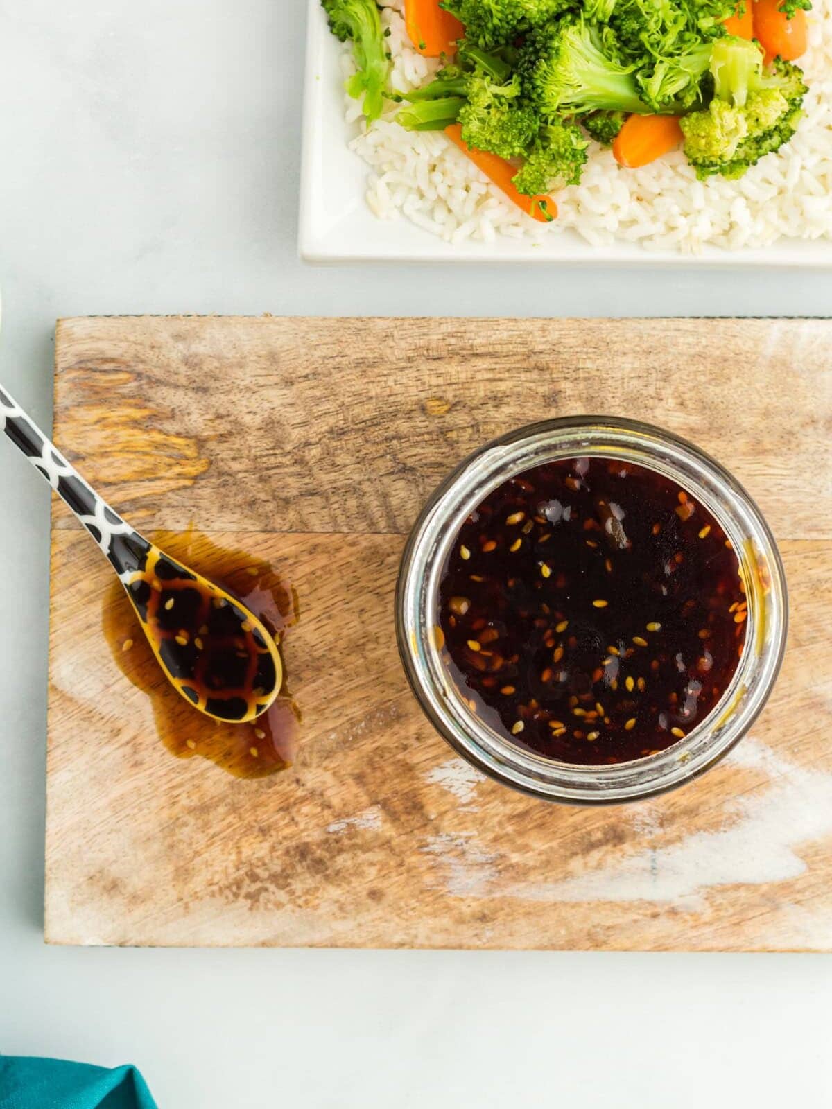 Overhead view of a glass jar filled with gluten free teriyaki sauce and a spoon on a wooden chopping board.