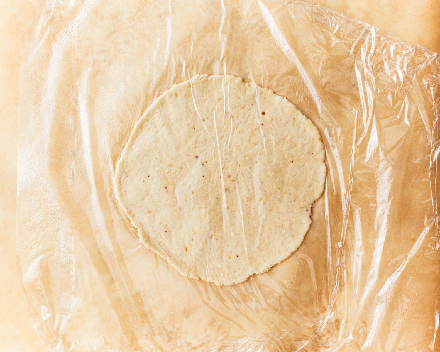 One portion of almond flour tortilla dough rolled out between parchment paper and plastic wrap.