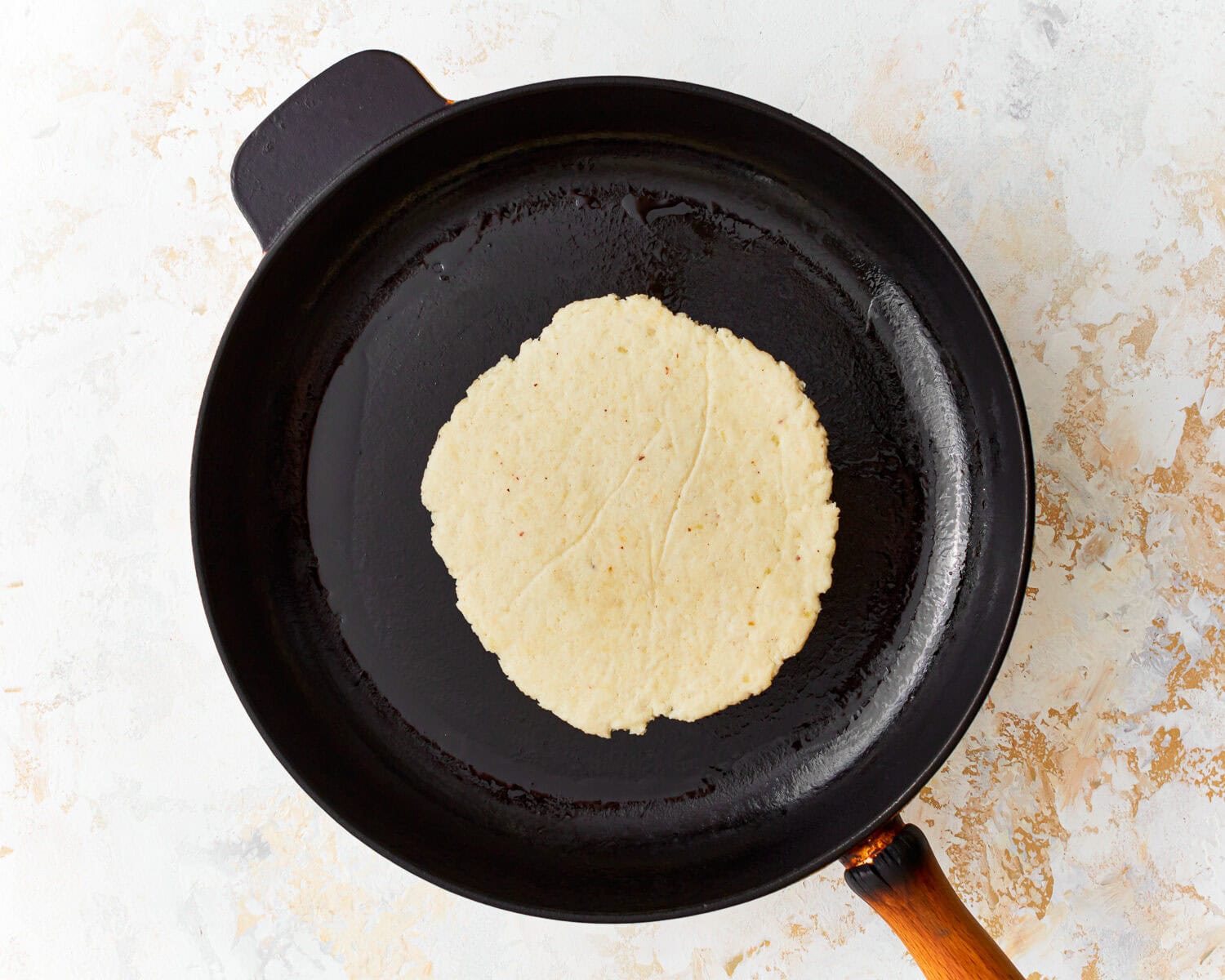 Overhead view of an almond flour tortilla cooking in a skillet.