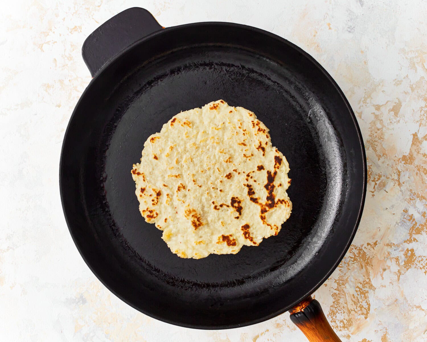 Overhead view of an almond flour tortilla cooking in a skillet.