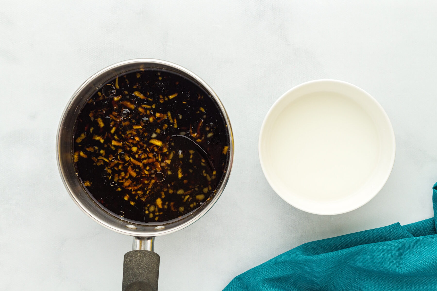 Overhead view of gluten free teriyaki sauce in a sauce pan next to a bowl of cornstarch slurry,