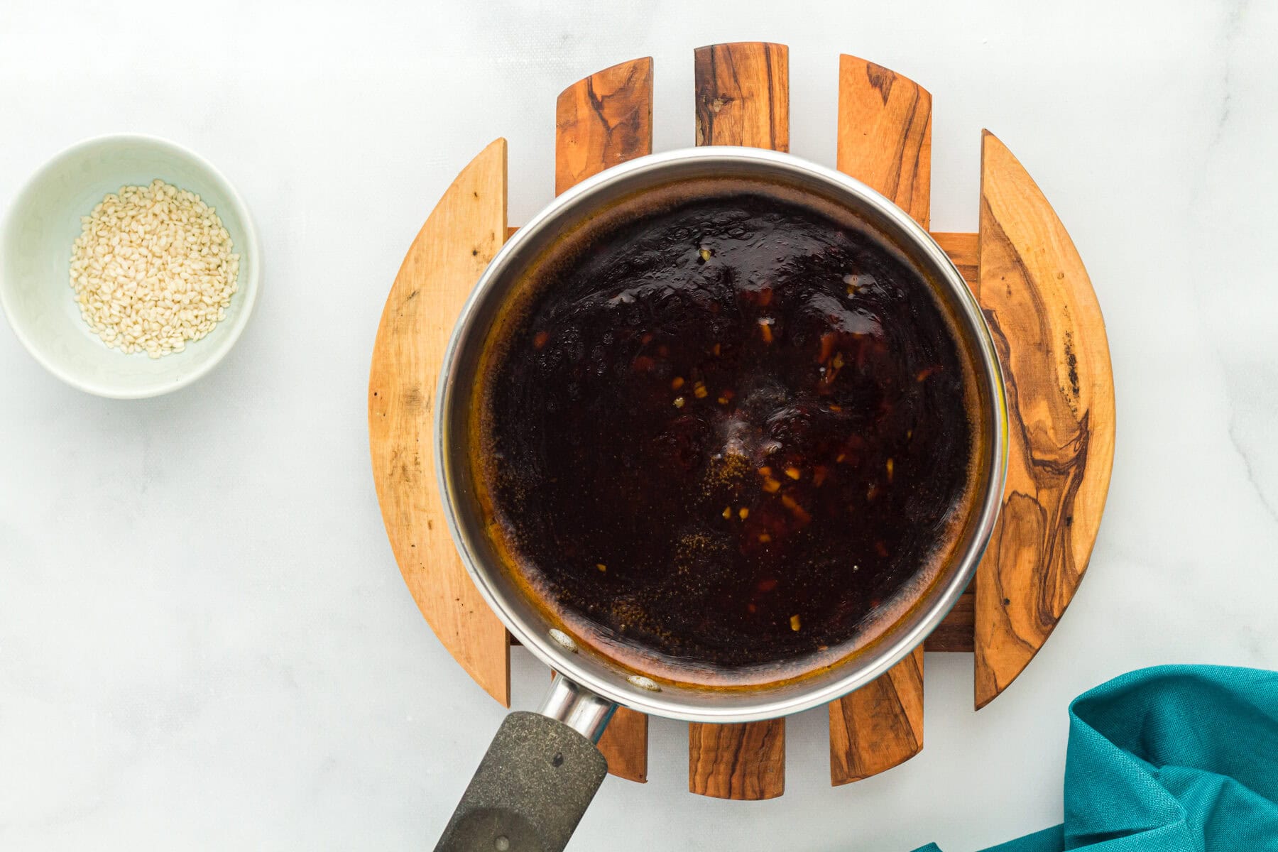 Overhead view of boiling gluten free teriyaki sauce in a saucepan next to a bowl of sesame seeds.