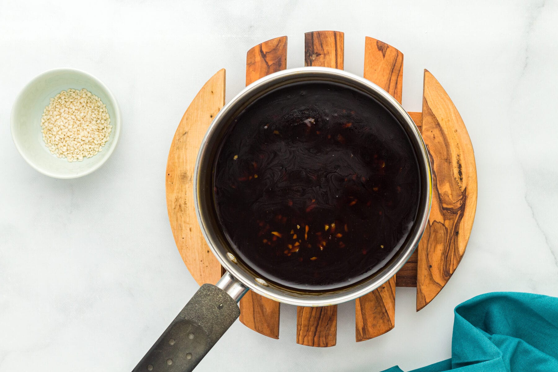 Overhead view of gluten free teriyaki sauce in a saucepan next to a bowl of sesame seeds.