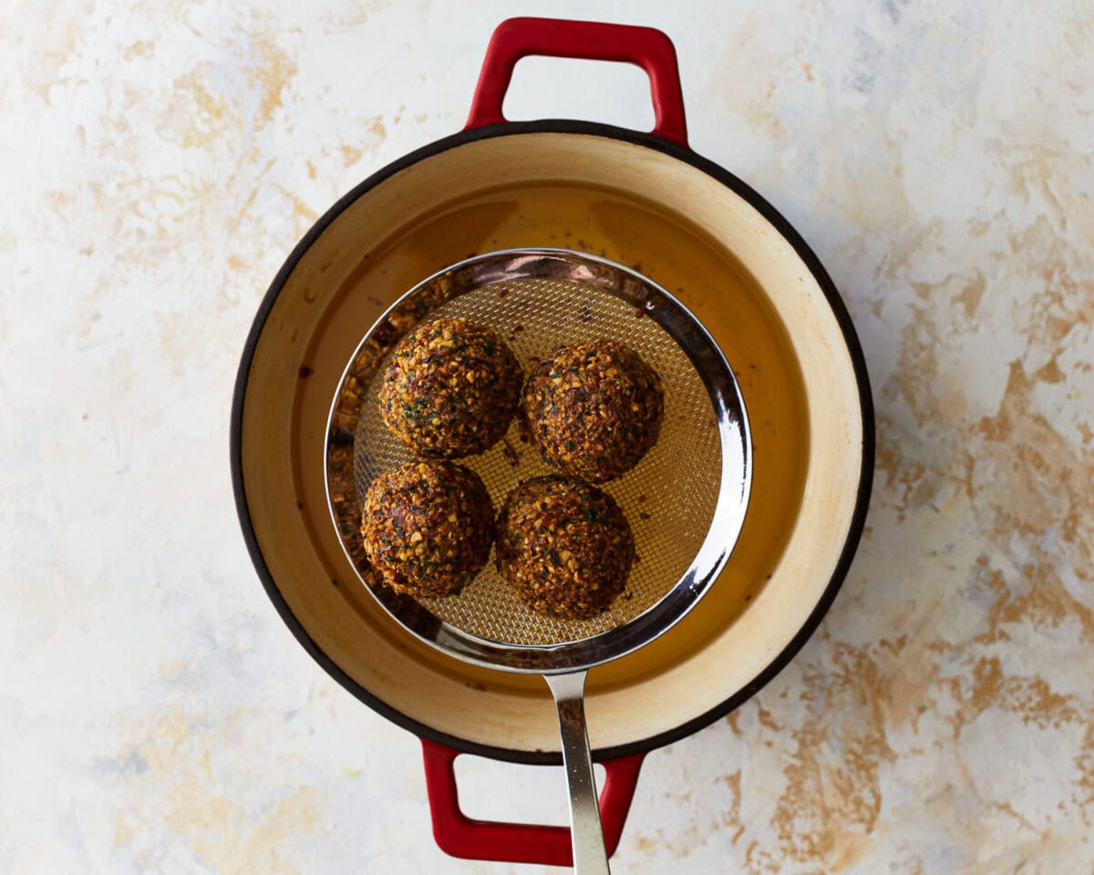 lifting 4 fried gluten-free falafel balls from a pot of oil.