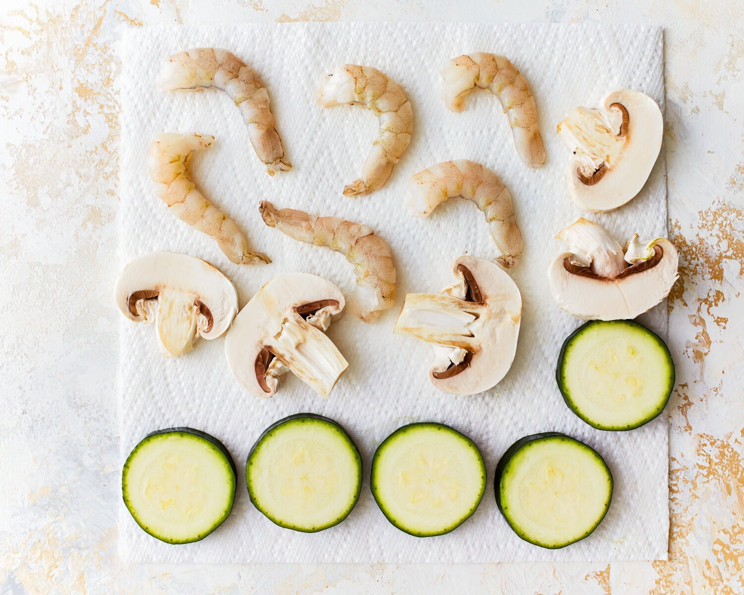 Sliced zucchini, mushrooms, and shrimp on a paper towel.