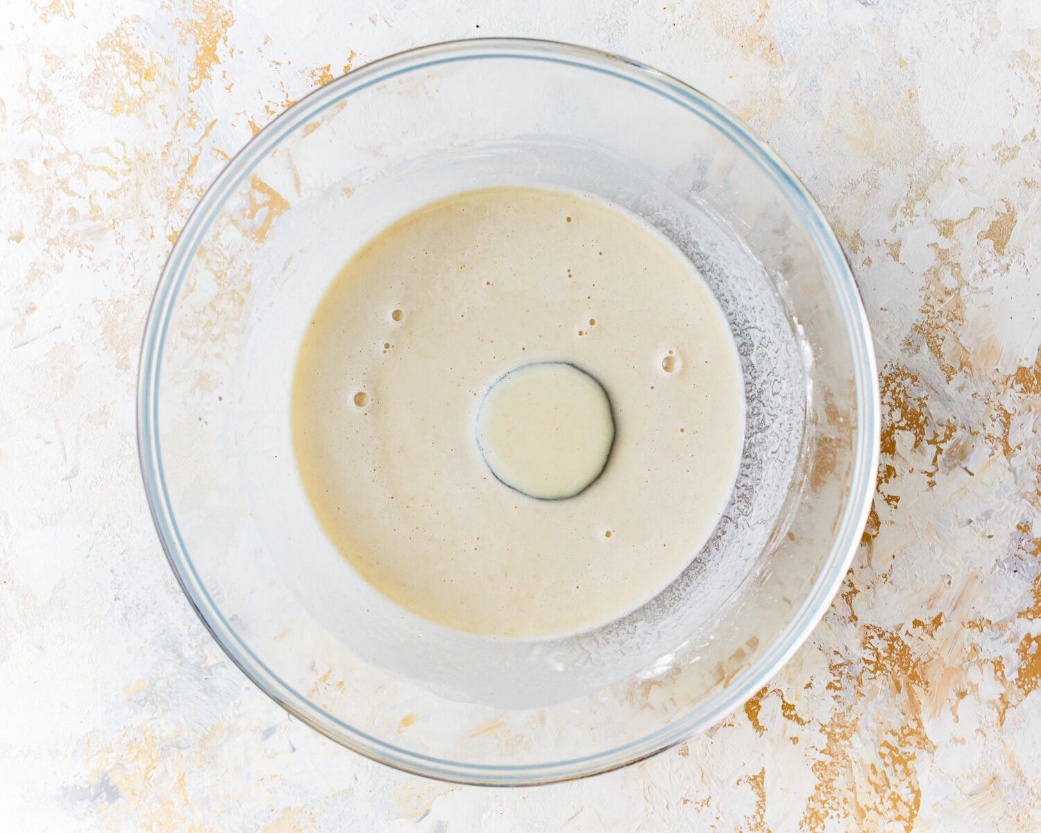 A slice of zucchini dipped in gluten free tempura batter in a glass mixing bowl.