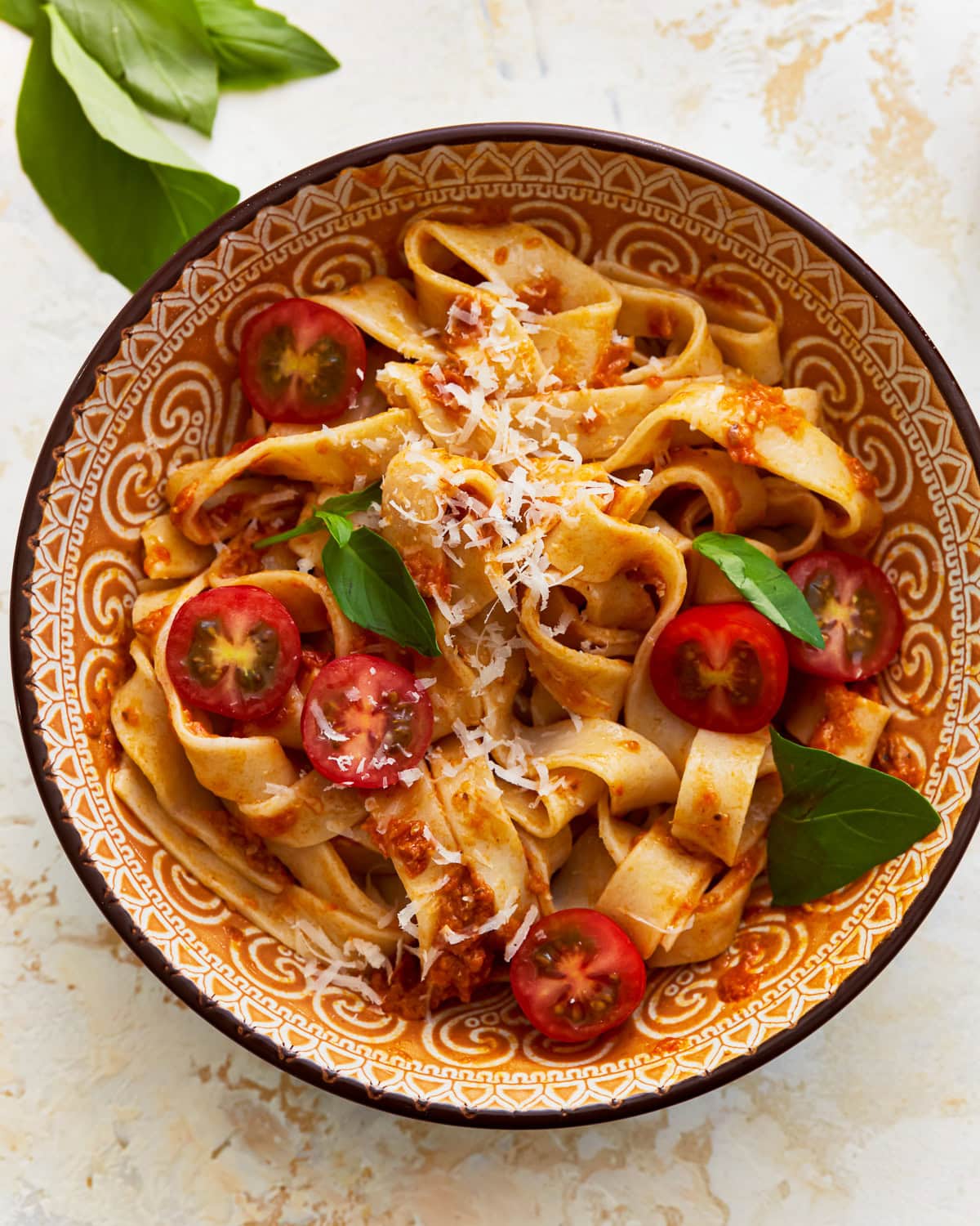 A bowl of almond flour pasta with fresh vegetables, shredded cheese, and herbs