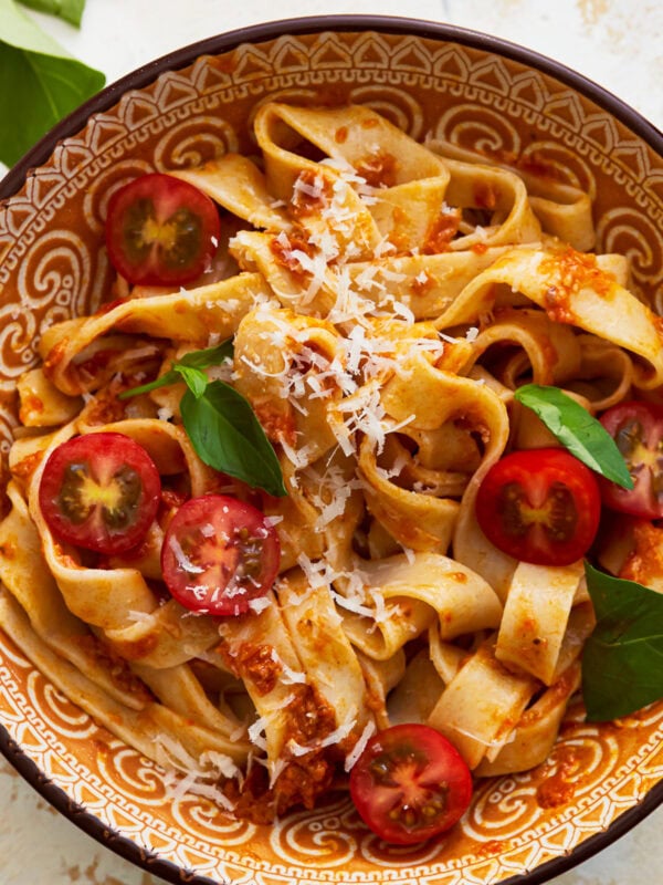 A close up of a bowl of almond flour pasta with fresh vegetables, shredded cheese, and herbs