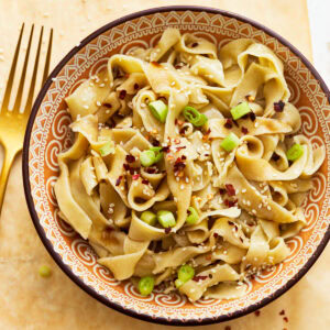 Gluten-free egg noodles in a bowl with green onions, sesame seeds, and red pepper flakes