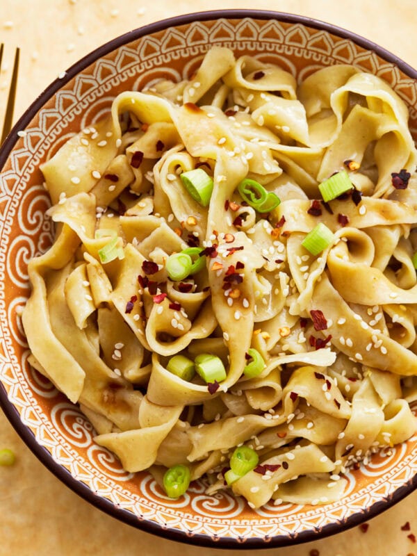 Gluten-free egg noodles in a bowl with green onions, sesame seeds, and red pepper flakes